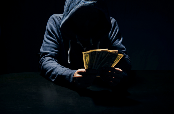 Un escroc portant un chandail à capuchon contemple des billets de banque qu’il tient dans ses mains