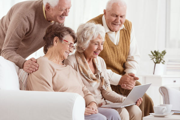 Image showing a group of four, happy looking, older individuals, two men and two women, all looking at one laptop on one of the laps of one of them women. 