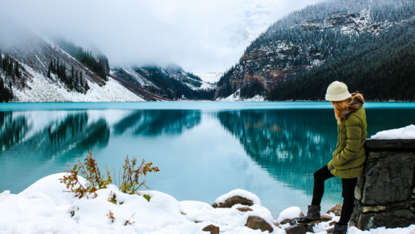 A woman stands next to Lake Louise at Banff National Park in Alberta during the winter.