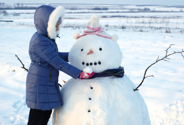 Une dame construit un grand bonhomme de neige rond.