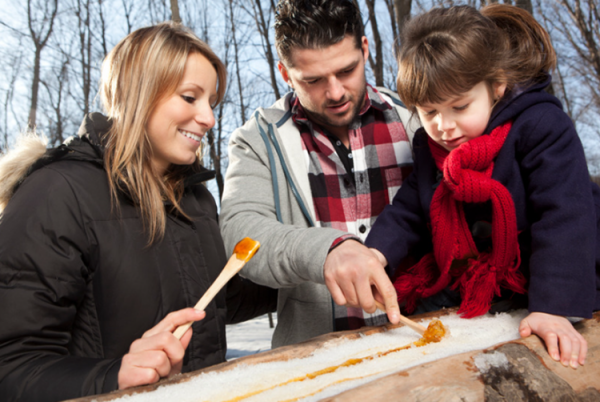 Une famille déguste de la tire sur la neige sur des bâtonnets de bois.