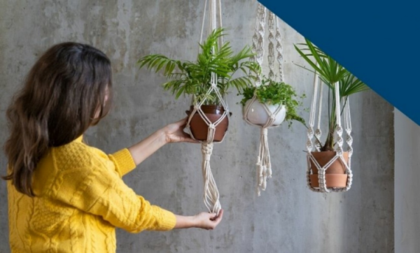 A woman is creating macramé -style plant hangers for her potted plants.