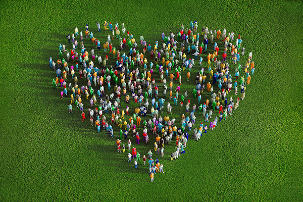 A large group of people standing outside on the grass forming the shape of a heart from a photo take above.