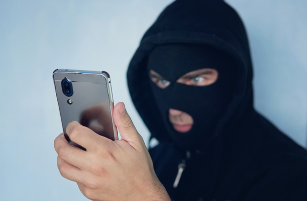 Un escroc en cagoule tient un téléphone cellulaire