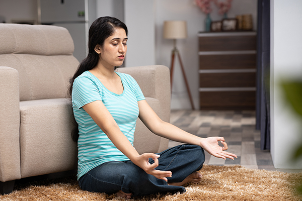 Woman meditating while sitting on a sofa at home