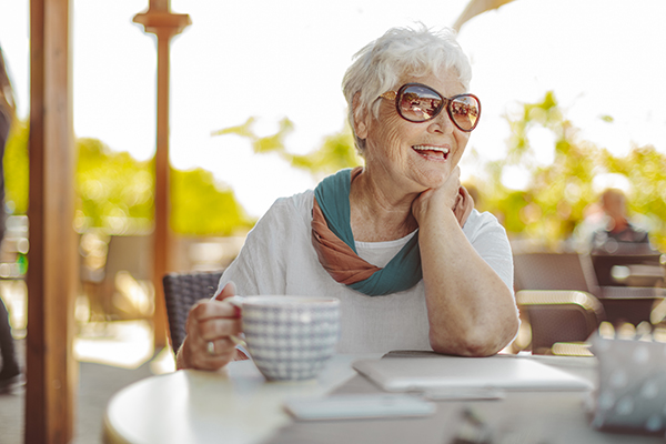 Mature woman sitting at a table smiling and enjoying a cup of tea.