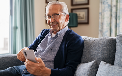 An older man, wearing glasses and smiling while browsing his smart phone