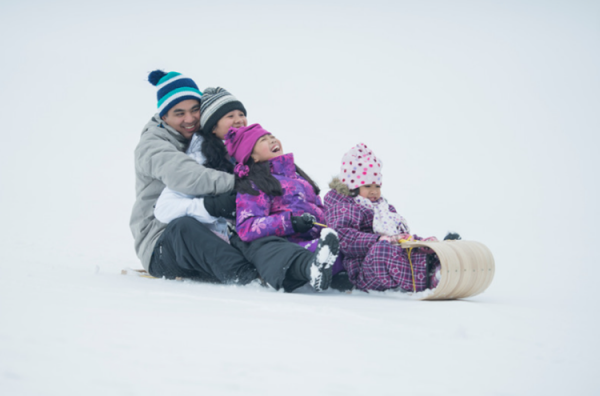A happy family sits on top of a wooden toboggan in the snow.