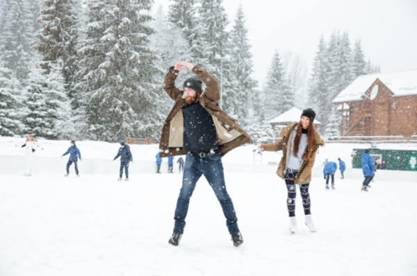 A young man and a young woman are enjoying ice skating on an outdoor rink.